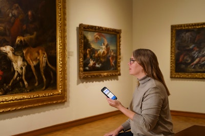 A museum visitor views an artwork in the European collection while listening to an audio guide on their phone.