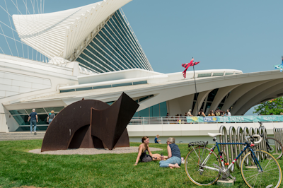 Various museum guests—a group of friends, a mother pushing a stroller, and an individual patron—approach the museum’s main entrance off Art Museum Drive.