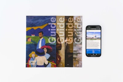 A stack of four museum collection guides sit to the left of a phone playing an audio guide. 